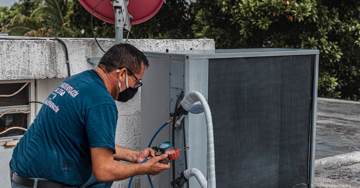 Installateur contrôlant une unité extérieure de climatisation devant une maison